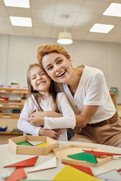 Insegnante positivo abbracciare allievo vicino materiale didattico nella scuola montessori — Foto stock