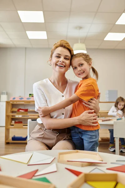 Positiver Schüler umarmt Lehrer und schaut in die Kamera in der Klasse der Montessori-Schule — Stockfoto