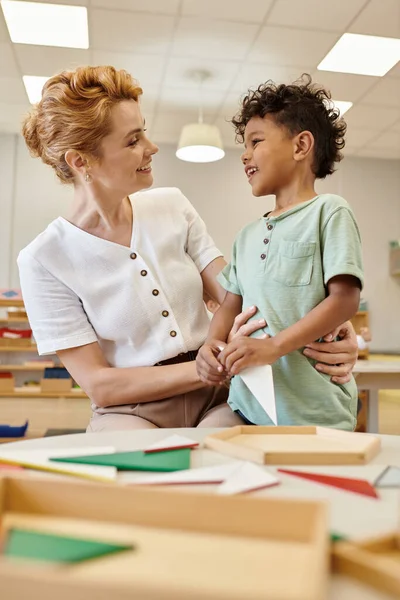 Enseignant positif parler à un garçon afro-américain en classe à l'école montessori — Photo de stock