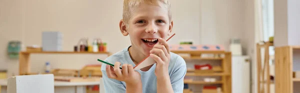 Joyeux garçon tenant des triangles pendant le jeu en classe à l'école montessori, bannière — Photo de stock