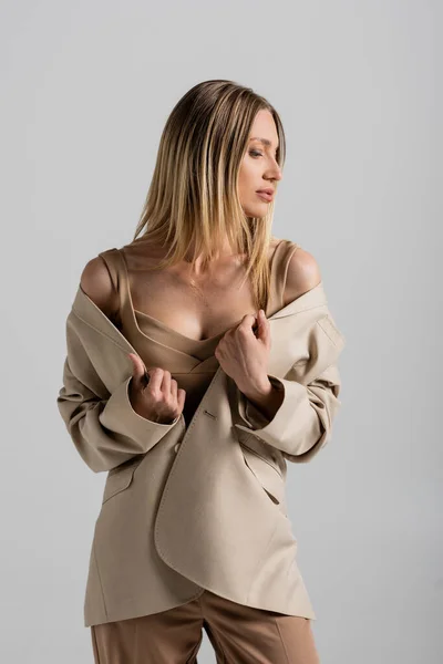 Nahaufnahme junge blonde Frau mit glattem Haar in beigem Kleid und Jacke vor grauem Hintergrund, Mode — Stockfoto