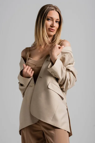 Ritratto di giovane donna bionda in abito elegante beige e giacca su sfondo grigio, stile e moda — Foto stock