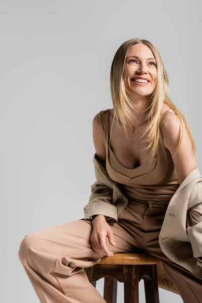 Крупним планом щаслива усміхнена блондинка в бежевому формальному костюмі, сидячи на стільці, концепція моди — стокове фото