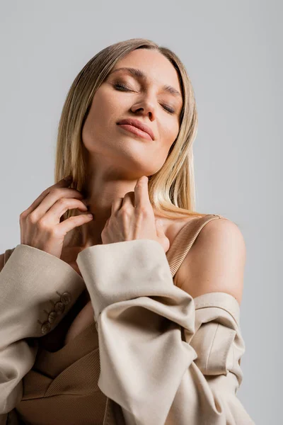 Portrait of smiling blonde woman in formal suit touching her chin on grey background, fashion — Stock Photo