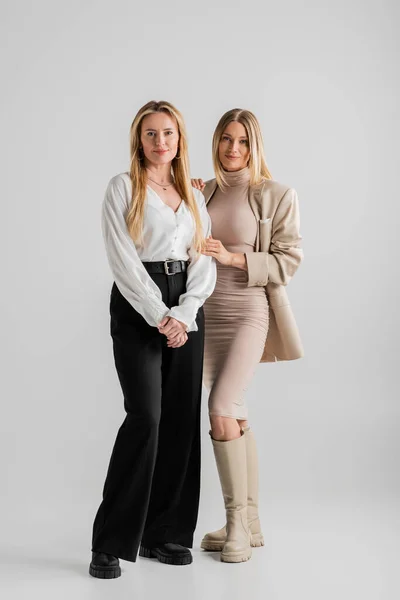 Привлекательные стильные сестры в формальной одежде, позирующие на сером фоне, сближение, концепция моды — стоковое фото
