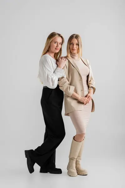 Attractive young woman posing with her hand on her sister's shoulder on grey backdrop, fashion — Stock Photo