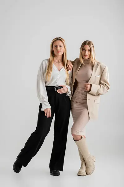 Eleganti sorelle bionde in abito formale in posa insieme su sfondo grigio, concetto di moda — Foto stock