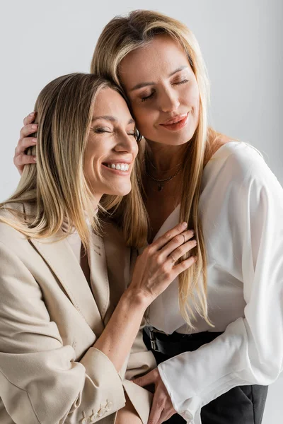 Две стильные привлекательные сестры в формальной одежде обнимающие друг друга и улыбающиеся, концепция моды — стоковое фото