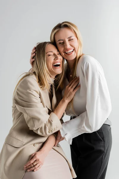 Two stylish blonde sisters in formal attire laughing and hugging each other, fashion concept — Stock Photo