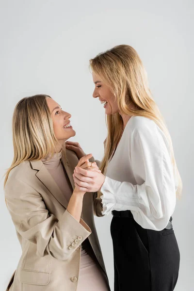 Stylish sisters in formal clothing smiling looking at each other and holding hands, fashion concept — Stock Photo