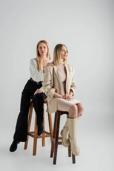 Attraenti sorelle eleganti in abbigliamento formale seduti su sedie, mano sulla spalla, moda e stile — Foto stock