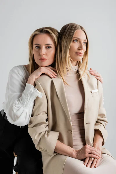 Two elegant pretty sisters in business casual attire sitting on chairs and hugging, fashion — Stock Photo