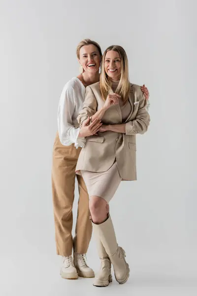 Two voguish sisters in formal pastel attire smiling sincerely and hugging, style and fashion — Stock Photo