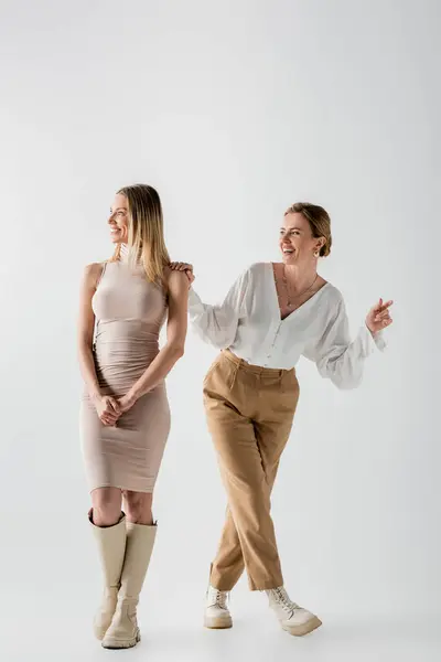 Cheerful stylish blonde sisters in pastel outfits smiling and looking away, style and fashion — Stock Photo