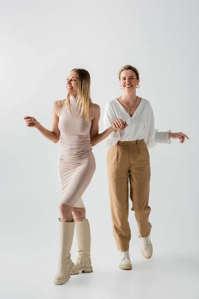 Trendige blonde Schwestern in pastellfarbenen Outfits, die lächeln und Händchen halten in Bewegung, Stil und Mode — Stockfoto