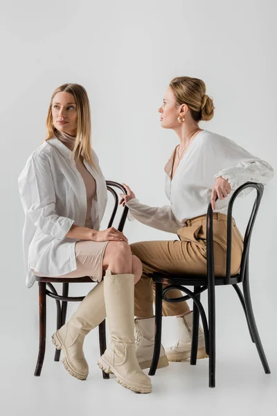 Due attraenti sorelle bionde in abbigliamento sedute su sedie e distogliendo lo sguardo, legame, moda — Foto stock