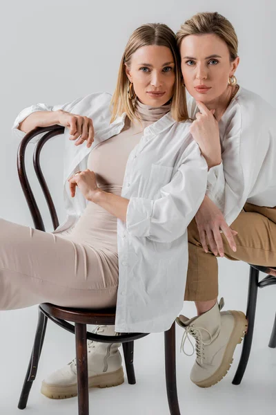 Stylish elegant blonde sisters sitting on chairs in fashionable pastel attire, fashion concept — Stock Photo