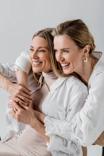 Two cheerful voguish sisters in formal wear hugging smiling and looking away, style and fashion — Stock Photo
