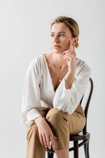 Красива блондинка в офіційному одязі, сидячи на стільці і торкаючись її обличчя, стилю і моди — стокове фото