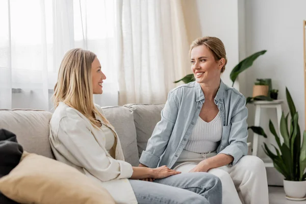 Attractive lovely sisters in casual outfit sitting on sofa and looking at each other, bond — Stock Photo