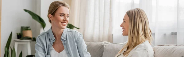 Two pretty charming sisters in casual attire sitting on sofa looking at each other, bonding, banner — Stock Photo