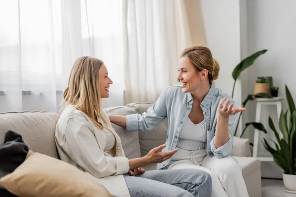 Gut aussehende Schwestern in lässiger Kleidung, die auf dem Sofa sitzen und miteinander reden, familiäre Bindung — Stockfoto