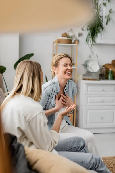 Две привлекательные сестры в повседневной одежде, сидя на диване, разговаривая и смеясь, семейные связи — стоковое фото