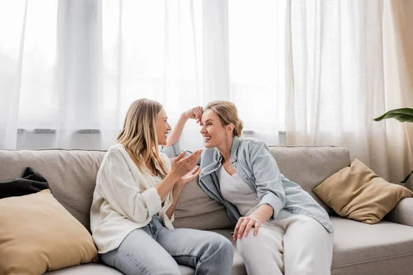 Zwei fröhliche schöne Schwestern, die auf dem Sofa sitzen und lächeln und miteinander reden, familiäre Bindung — Stockfoto