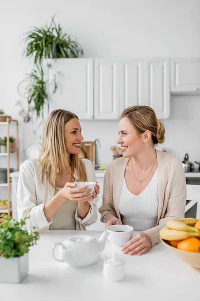 Закрыть две сестры, сидящие за столом, пьющие чай и улыбающиеся друг другу, семейные связи — стоковое фото