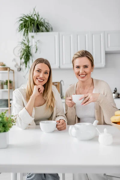 Close up duas irmãs em roupa pastel beber chá sorrindo e olhando para a câmera, ligação familiar — Fotografia de Stock