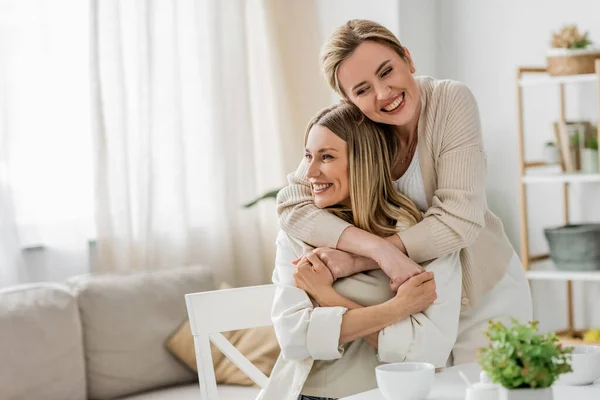 Lovely pretty sisters in trendy attire hugging and smiling sincerely on kitchen backdrop, bonding — Stock Photo
