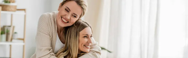 Pretty sisters in trendy attire hugging and smiling sincerely on kitchen backdrop, bonding, banner — Stock Photo