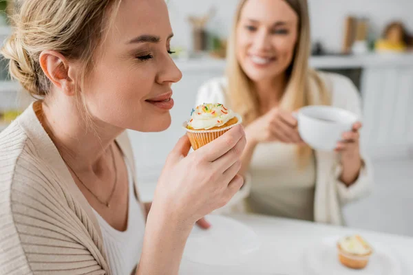Close up two trendy sisters sitting at table drinking tea and eating cupcakes, closed eyes, bonding — Stock Photo