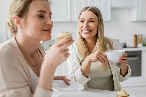Close up two beautiful sisters in casual wear tasting cupcakes and drinking tea, family bonding — Stock Photo