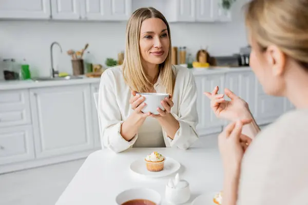 Обрезанный вид красивых сестер говорить и наслаждаться чаем с кухонным фоном, связи — стоковое фото
