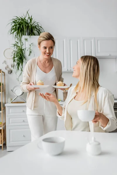Duas irmãs em adorável traje pastel conversando e sorrindo, cupcakes em mãos, ligação familiar — Fotografia de Stock