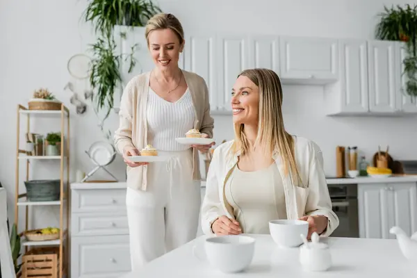 Duas irmãs loiras de boa aparência em cardigans pastel sorrindo e olhando para longe, ligação familiar — Fotografia de Stock