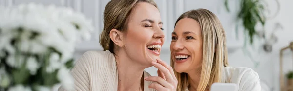 Two blonde sisters in lovely attire laughing and holding mobile phone, family bonding, banner — Stock Photo