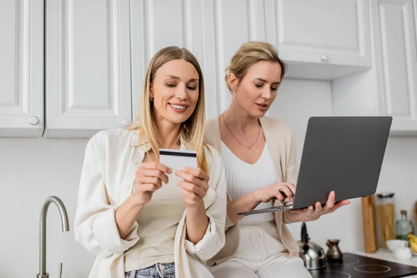 Good looking lovely sisters in trendy pastel attire holding credit card and laptop, family bonding — Stock Photo