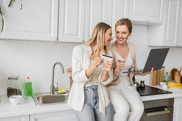 Deux jolies soeurs blondes avec ordinateur portable et carte de crédit se regardant, liens familiaux — Photo de stock