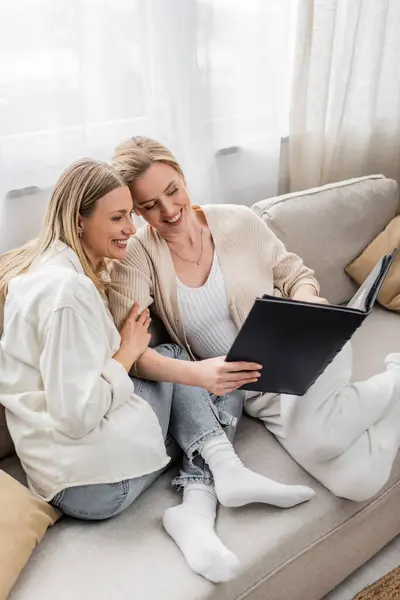 Deux charmantes sœurs en tenue pastel décontractée regardant l'album photo, ensemble, liens familiaux — Photo de stock