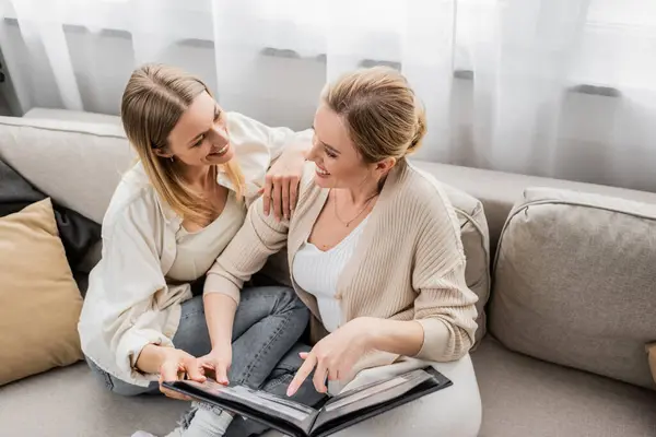 Happy attractive sisters in casual lovely attire holding photo album looking at each other, bonding — Stock Photo