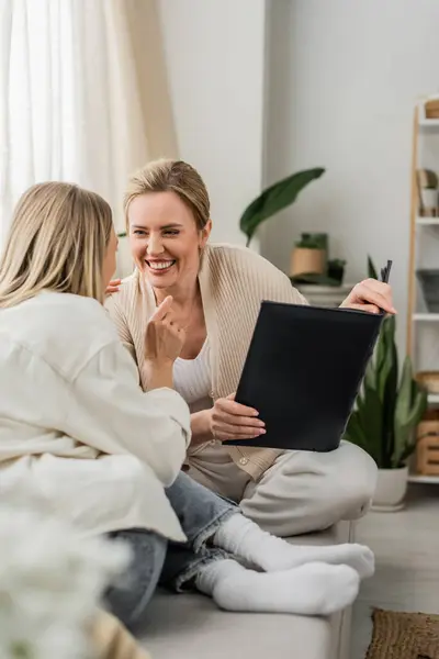 Joyful attractive sisters in lovely outfits laughing and holding photo album, family bonding — Stock Photo