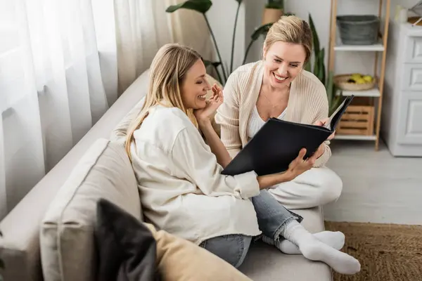 Beautiful charming sisters smiling and looking at photo album, hand to chin, family bonding — Stock Photo