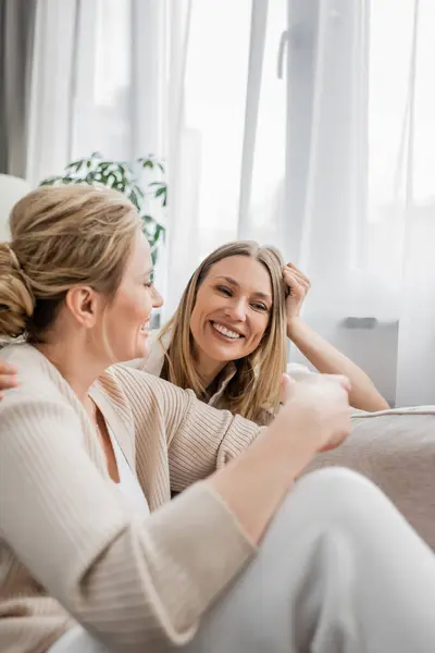 Close up trendy lovely sisters sitting on sofa smiling sincerely at each other, family bonding — Stock Photo