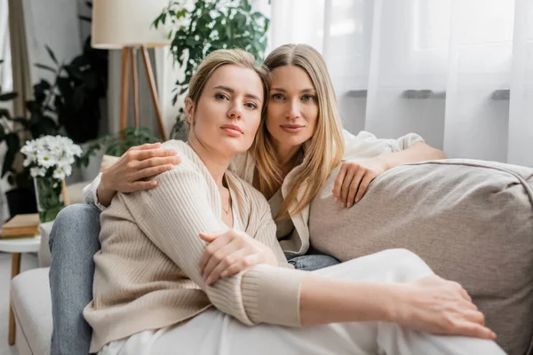 Portrait of pretty lovely sisters sitting on sofa hugging and looking at camera, family bonding — Stock Photo