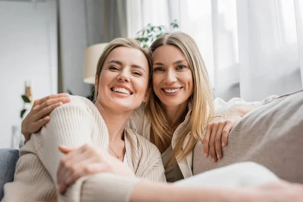 Zwei fröhliche trendige Schwestern in pastellfarbenen Strickjacken, die aufrichtig in die Kamera lächeln, familiäre Bindung — Stockfoto