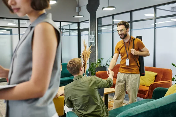 Pleased bearded man shaking hands with business partner near blurred businesswoman in modern office — Stock Photo