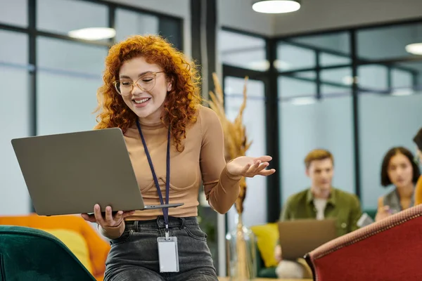 Успешная рыжая деловая женщина с ноутбуком рядом размытый коллега в современном офисном пространстве — стоковое фото