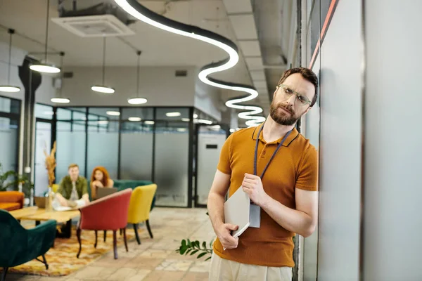 Расстроенный бородатый предприниматель с документами и закрытыми глазами, размытые коллеги разговаривают в офисе — стоковое фото